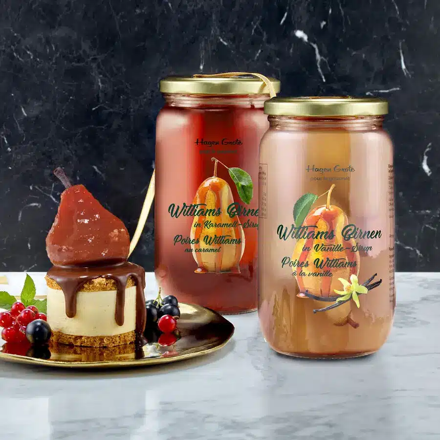 Zwei Gläser Williams-Birnen in Karamellsirup und Vanillesirup, daneben ein Dessertteller mit Birne, Schokoladenguss, Beeren und Minze.