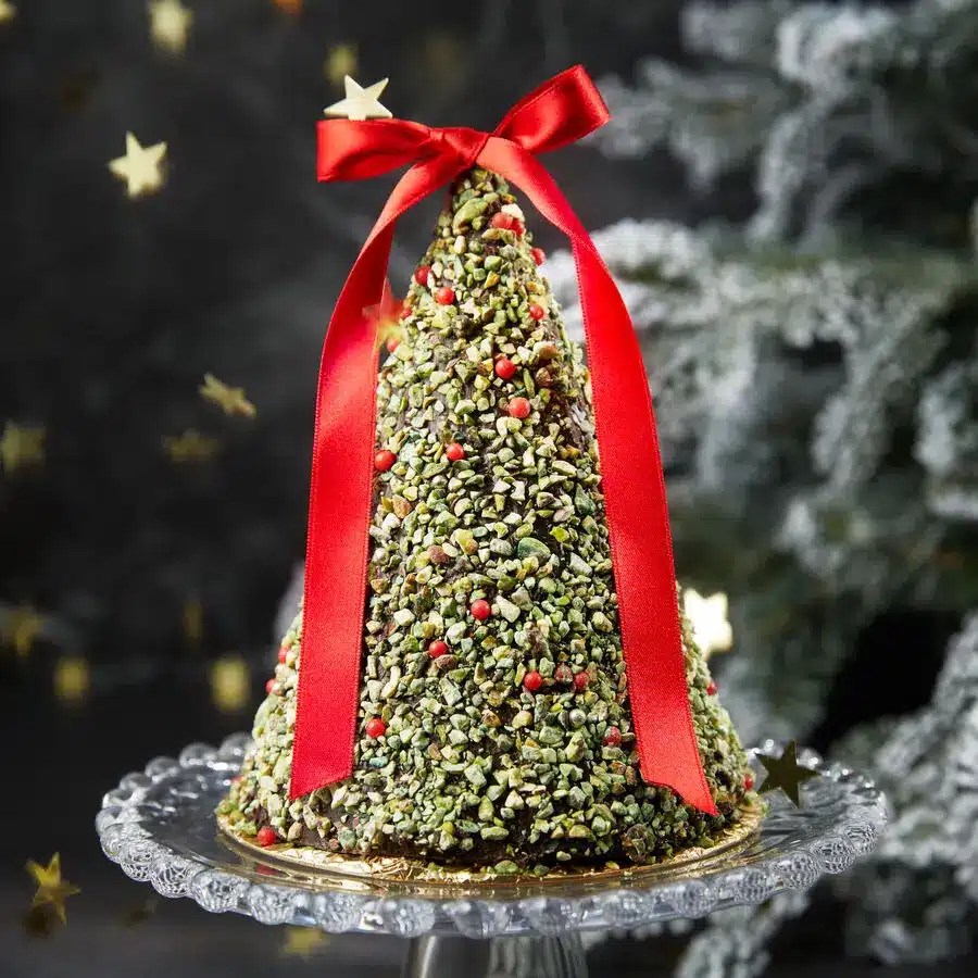 Dreidimensionaler Schokoladen-Tannenbaum mit Pistazien und roter Schleife, festlich dekoriert auf Glasplatte