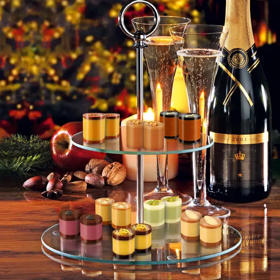 Feine Dessertauswahl in bunten Schälchen auf Etagere mit Champagner, festlich serviert