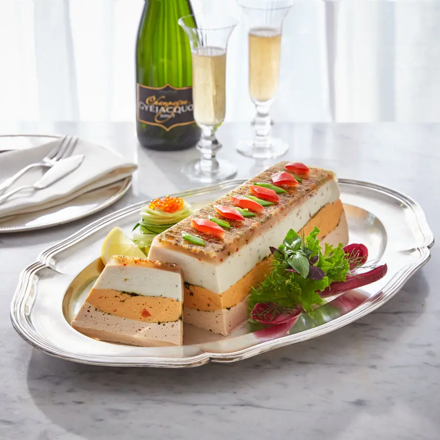 Festliche Fischterrine mit Gemüse, garniert und serviert auf Silberplatte mit Champagner