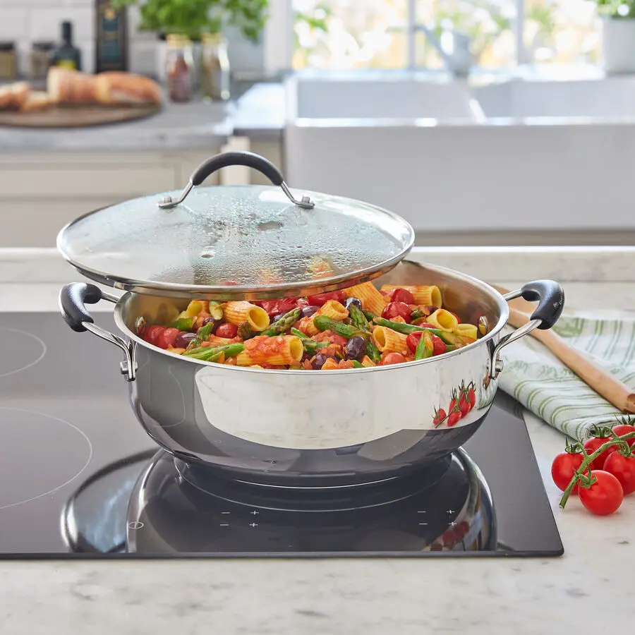 Edelstahl-Kochtopf mit Glasdeckel, gefüllt mit Pasta, Gemüse und Tomatensauce auf Herdplatte