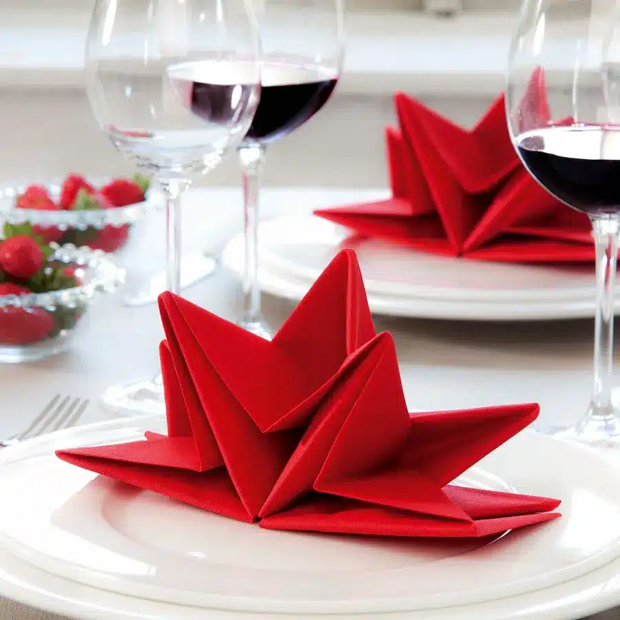 Rote Stoffservietten kunstvoll als Stern gefaltet, festliche Tischdekoration mit Weingläsern