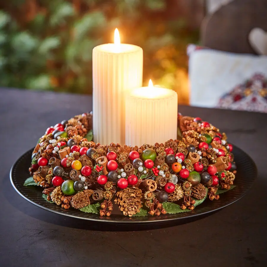 Adventskranz mit bunten Beeren, Zapfen und zwei weißen Stumpenkerzen als festliche Tischdekoration zu Weihnachten