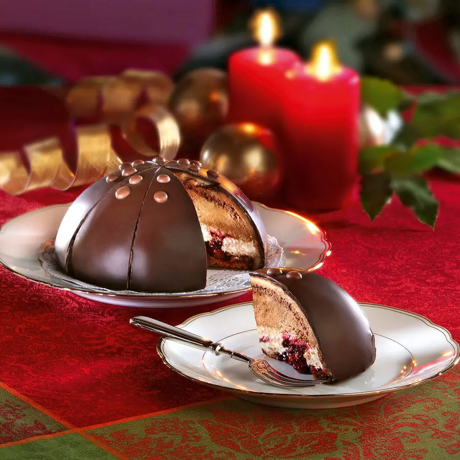 Halbkugelförmige Schokoladentorte mit Creme- und Beerenschichten, angeschnitten auf festlich gedecktem Tisch.