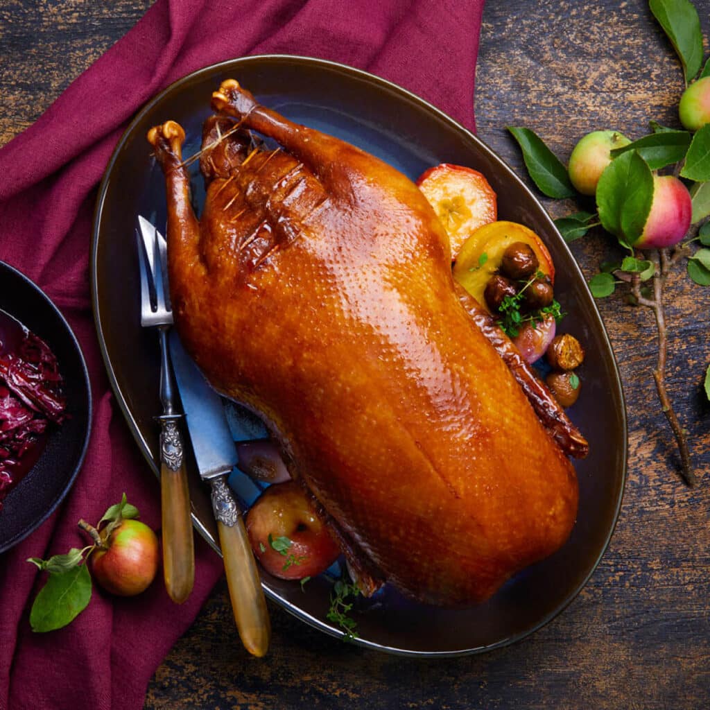 Knusprig gebratene Weihnachtsgans auf festlicher Platte mit Äpfeln, herbstlich dekoriert als klassisches Festtagsgericht