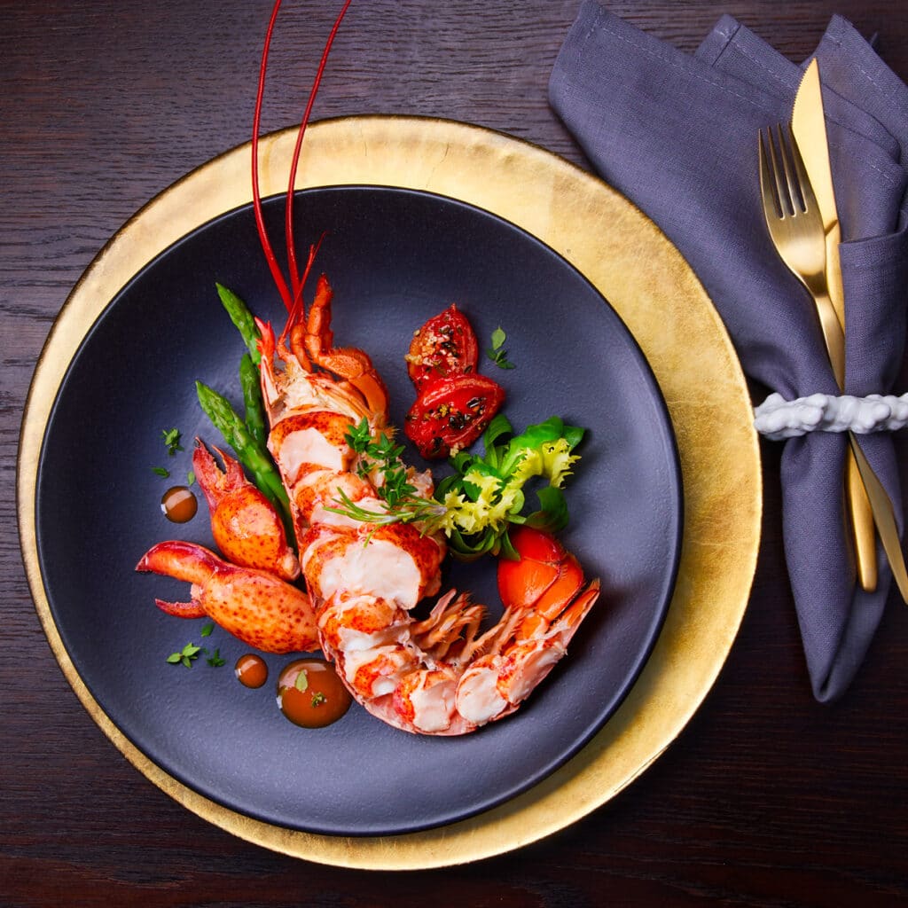 Edler Hummer mit Spargel, Tomaten und Kräutern auf elegantem Weihnachtsteller.