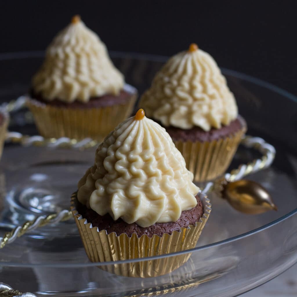 Schokoladen-Cupcakes mit üppigem weißen Creme-Topping in Tannenbaumform, goldene Förmchen, festliche Deko