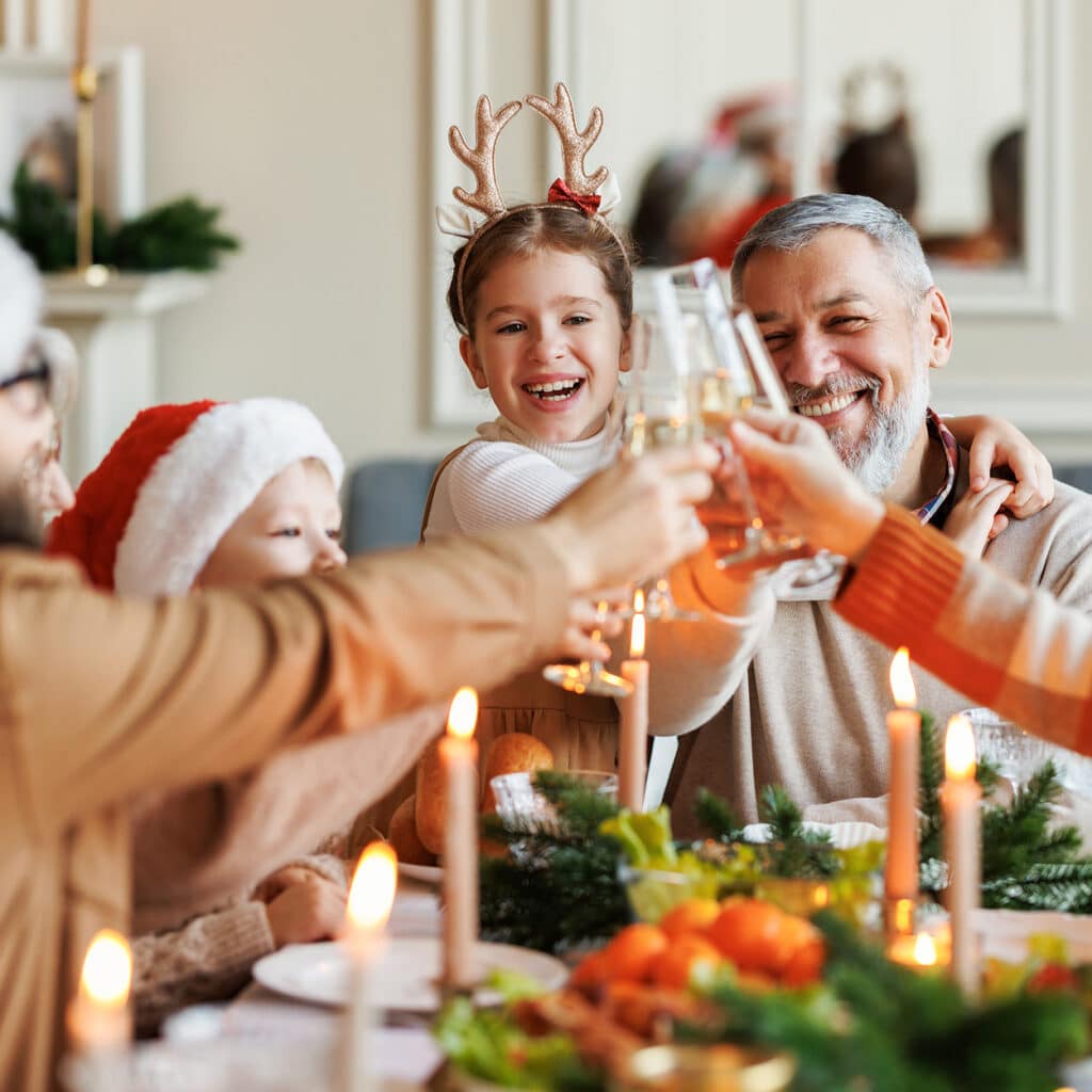 Familie stößt an Heiligabend am festlich geschmückten Tisch mit Kerzen und Essen an