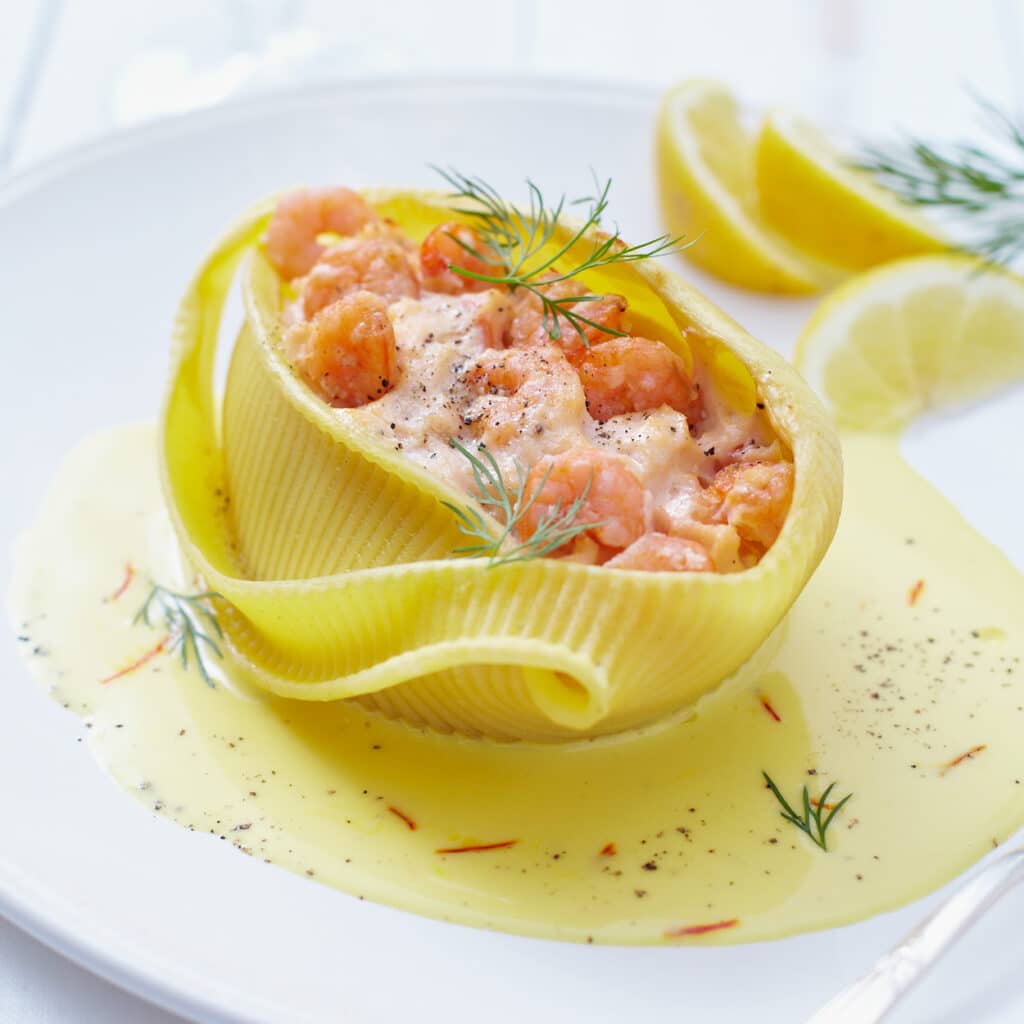 Caccavelle-Muschelnudel mit Garnelenfüllung in cremiger Safransauce, festlich angerichtet mit frischem Dill und Zitrone