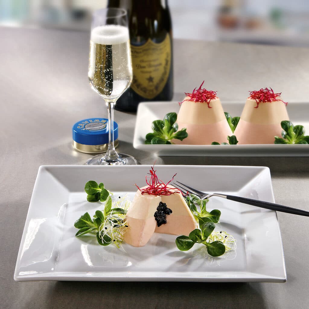 Edle Vorspeise mit Foie gras und Kaviar, dekoriert mit Salat und Sprossen, serviert mit Champagner im Hintergrund