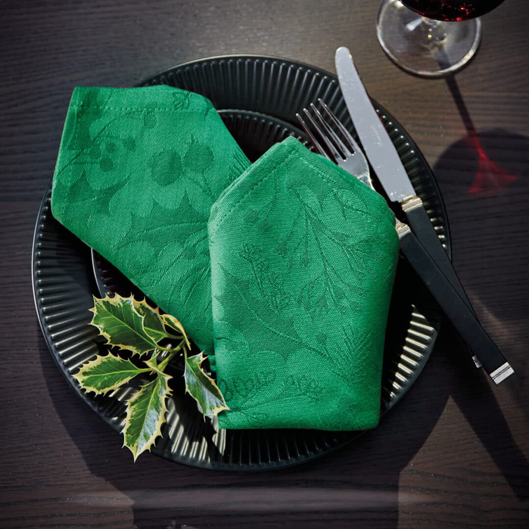 Schwarzer Teller mit grüner Stoffserviette und Ilexzweig, festlich gedeckt
