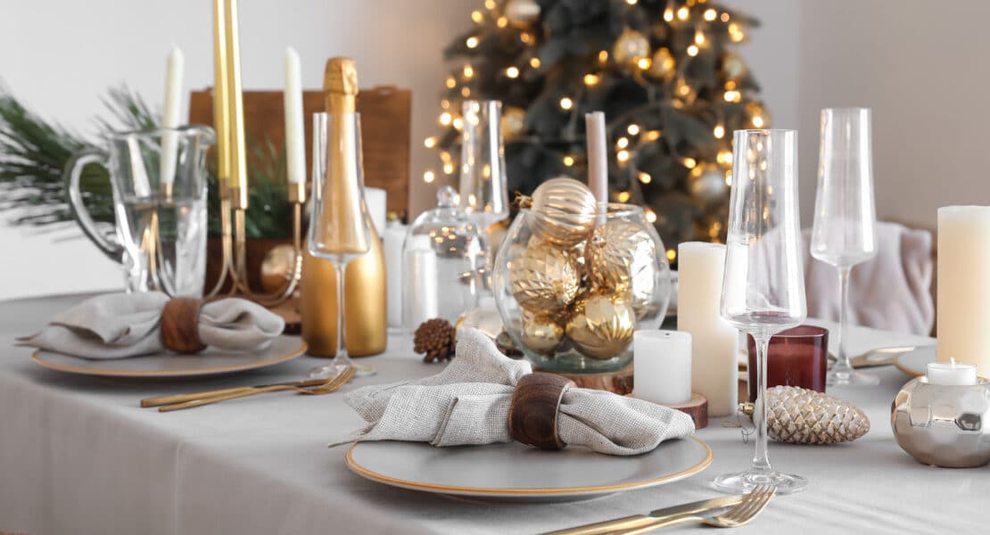 Festlich gedeckter Tisch in Gold und Weiß mit Kerzen, Gläsern und Tannenzweigen