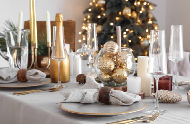 Festlich gedeckter Tisch in Gold und Weiß mit Kerzen, Gläsern und Tannenzweigen