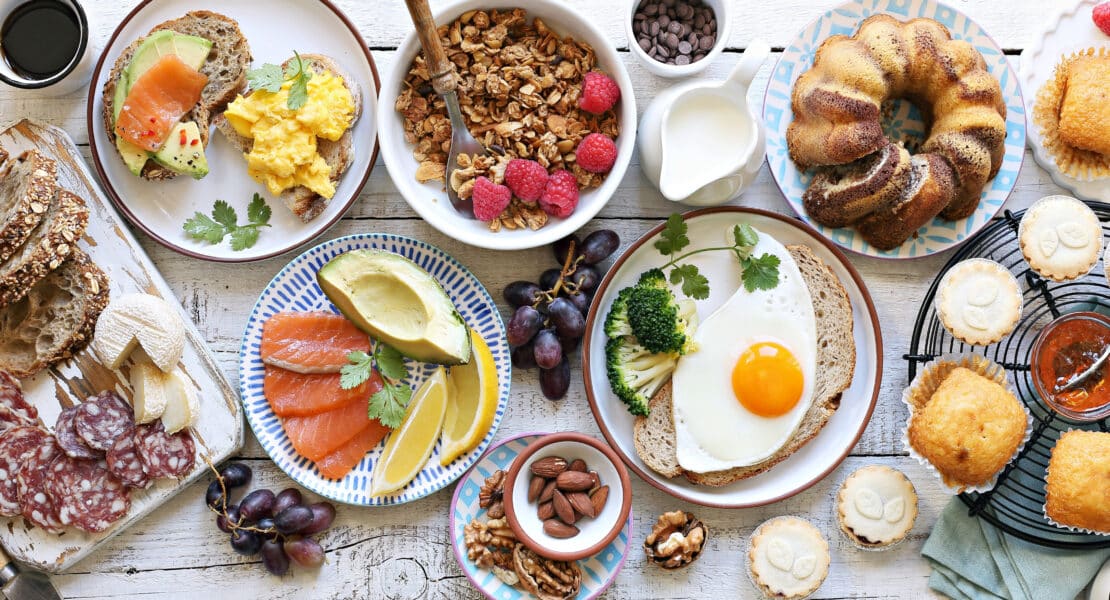 Frühstücks-Spread mit Avocado-Lachs-Brot, Rührei, Spiegelei auf Brot, Müsli mit Himbeeren, Kuchen und Gebäck