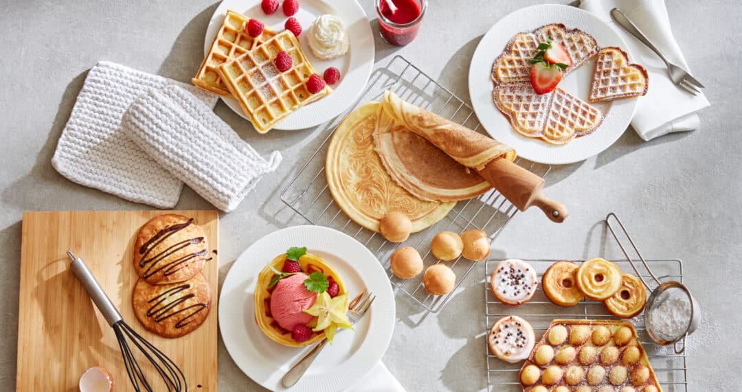S&uuml;&szlig;e Brunch-Auswahl mit Waffeln, Cr&ecirc;pes, Geb&auml;ck, Desserts und Puderzucker auf heller Tischfl&auml;che