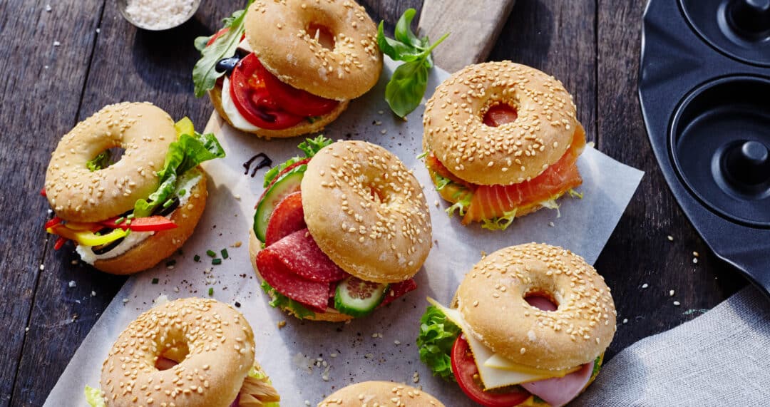Belegte Mini-Bagels mit Sesam, Tomate, Salat, K&auml;se, Wurst und Lachs auf Backpapier