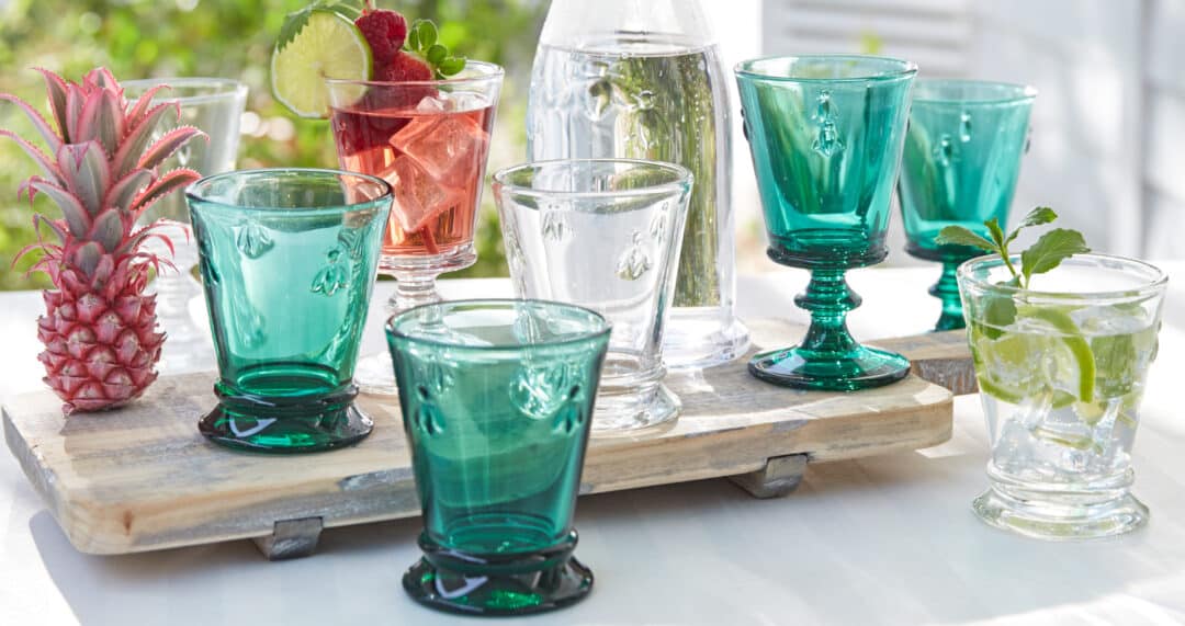 Verschiedene Trinkgl&auml;ser und Kelche auf Tablett, daneben ein Getr&auml;nk mit Eis, Limette und Beeren sowie eine Ananas