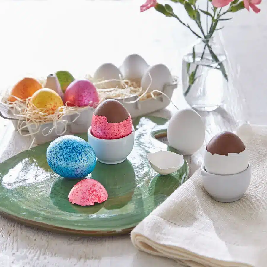 Bunt gefärbte Ostereier und Schokoladeneier in Eierbechern auf frühlingshaft gedecktem Ostertisch