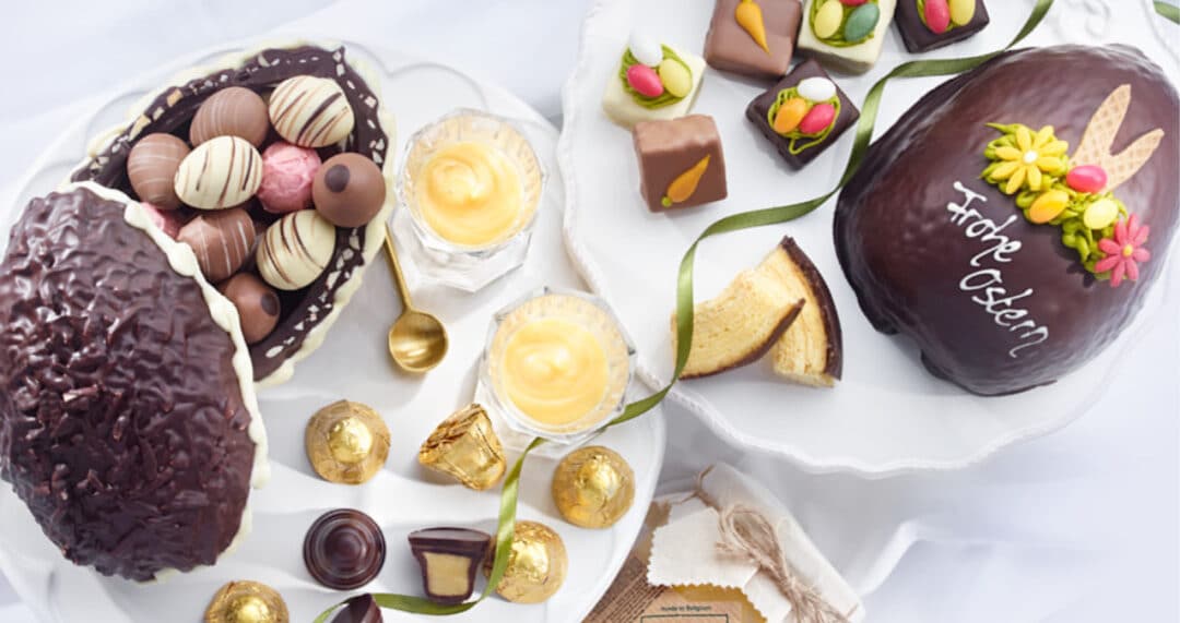 Verschiedene Osterpralinen, Ostergebäck und gefüllte Ostereier auf weißen Tellern arrangiert