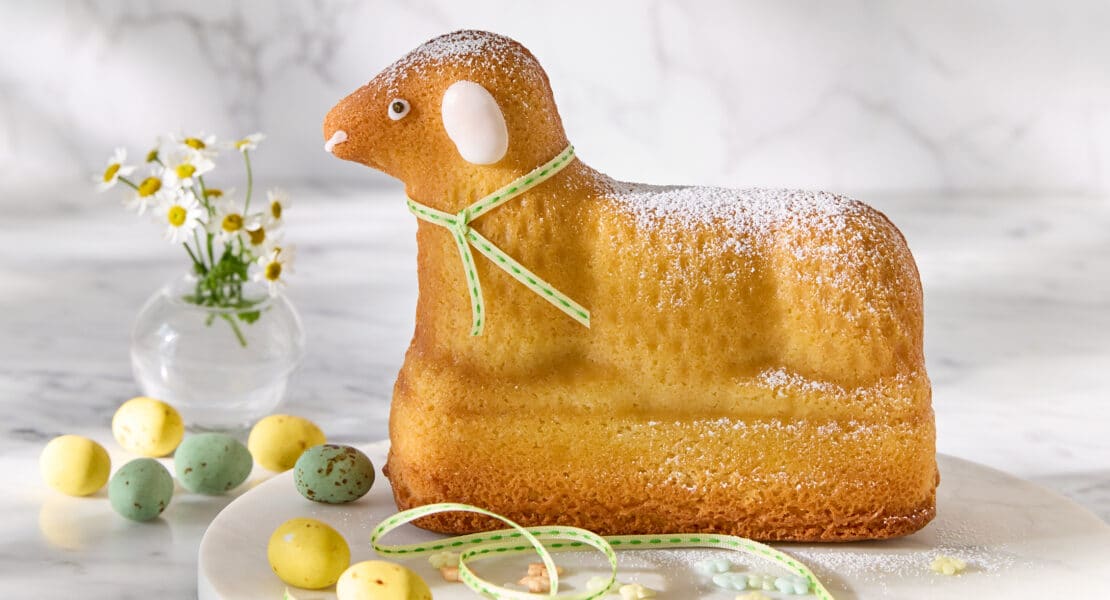 Klassisches Osterlamm aus Rührteig, mit Puderzucker bestäubt, auf heller Platte serviert