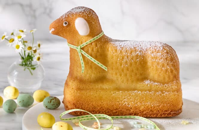 Klassisches Osterlamm aus Rührteig, mit Puderzucker bestäubt, auf heller Platte serviert