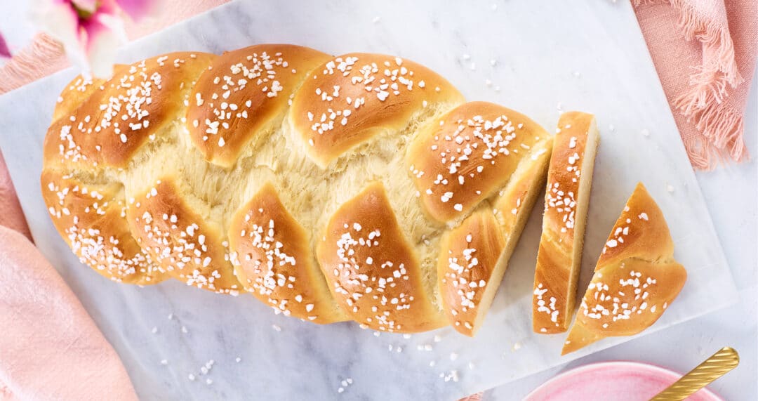 Hefezopf auf Marmorbrett, angeschnitten und mit Hagelzucker bestreut.