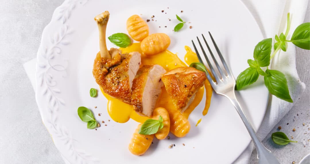 Perlhuhnbrust mit S&uuml;&szlig;kartoffel-Gnocchi und S&uuml;&szlig;kartoffel-Safran-Sauce auf wei&szlig;em Teller angerichtet.