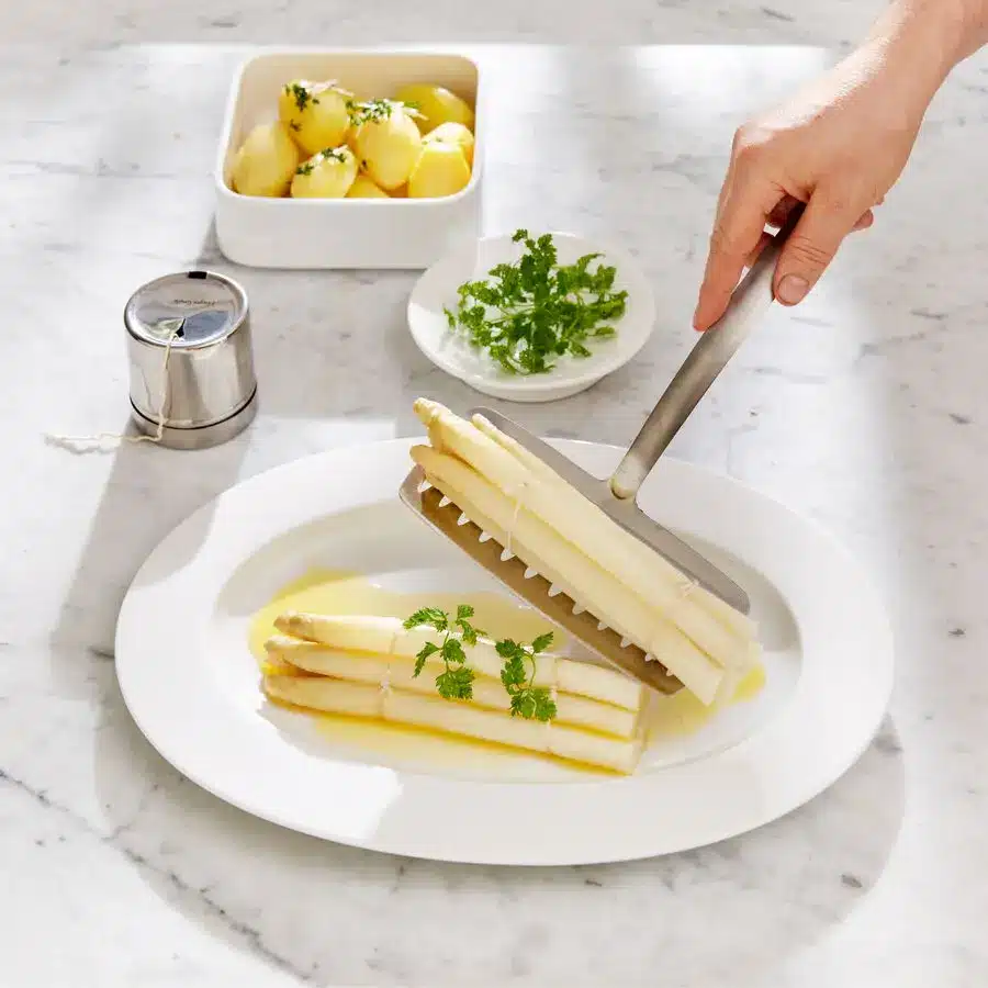 Edelstahl-Spargelheber hebt wei&szlig;e Spargelstangen schonend auf einen Teller mit Sauce Hollandaise