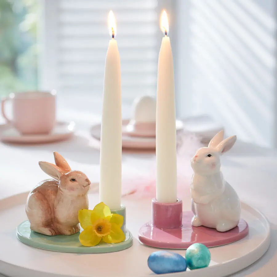 Kerzenhalter mit Hasen in Pastellfarben auf gedeckter Ostertafel mit brennenden Kerzen