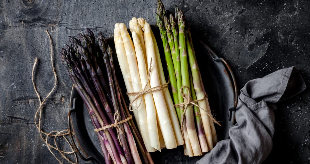 Violetter, weißer und grüner Spargel gebündelt auf einer rustikalen Platte mit Leinentuch